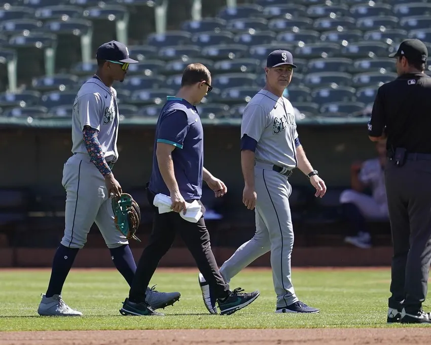 Le joueur de champ central Julio Rodriguez des Seattle Mariners, à gauche, quitte le terrain avec le manager Scott Servais, au milieu à droite, et un entraîneur pendant la première manche d'un match de baseball contre les Oakland Athletics à Oakland, en Californie, Jeudi 22 septembre 2022.