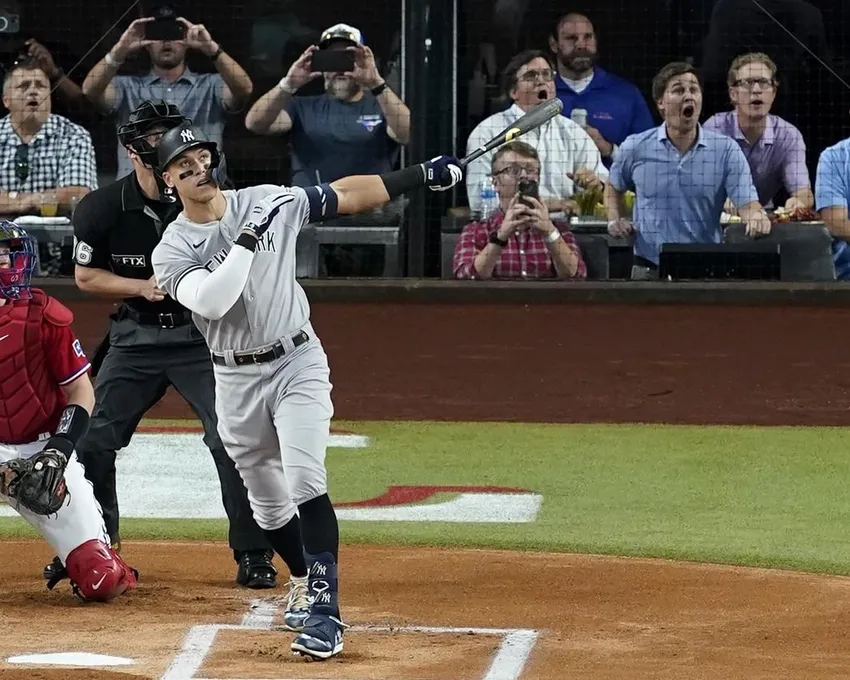 Aaron Judge, des Yankees de New York, poursuit son home run en solo, son 62e de la saison, alors que le receveur des Rangers du Texas, Sam Huff, à gauche, et l'entraîneur de l'équipe de hockey, à droite, sont à l'œuvre. Avec ce home run, Judge a établi le record AL de home runs en une saison, dépassant Roger Maris.