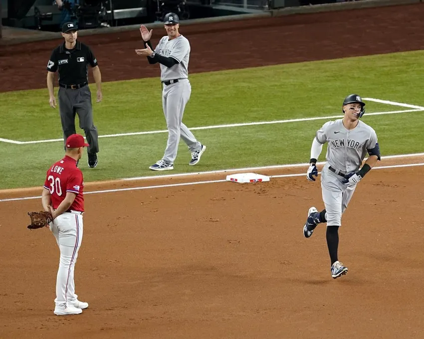 Aaron Judge, des Yankees de New York, contourne les bases en passant devant le joueur de première base Nathaniel Lowe (30) des Texas Rangers, l'arbitre Lew Williams et la première base des Yankees. Avec ce home run, Judge a établi le record AL de home runs en une saison, dépassant Roger Maris.
