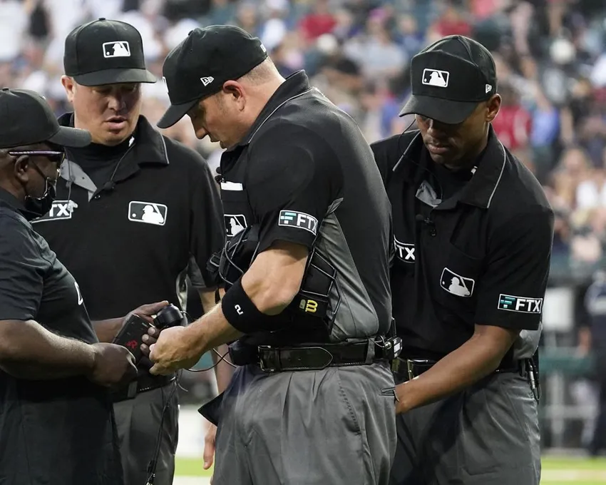 Kelvin Pickens de MLB Network, à gauche, inspecte la radio et le casque pour un appel lors d'une révision de jeu avec les arbitres Cory Blaser, deuxième à partir de la gauche, Edwin Moscoso, à droite, et Dan Bellino après la première manche d'un match de baseball à Chicago, vendredi 22 juillet 2022. Après un siècle et demi de Major League Baseball - après des générations de grognements et de grondements, de cris étouffés et de gestes spectaculaires des bras, et un sentiment cultivé d'éloignement - quelque chose de tranquillement extraordinaire est arrivé au passe-temps national cette année : Les arbitres ont commencé à parler au monde.